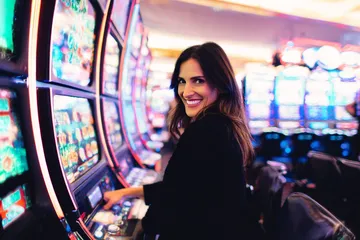 A woman smiling by bright slot machines showing lucky symbols, showcasing the exciting slot offerings at PHCHARMS.